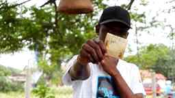 A man in a black cap showing fifty cedis note